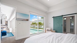 A bedroom with a large bed, a sliding glass door to a pool area, and a teal door. - Paradise Found 3 Bedroom Home by RedAwning (Sarasota)