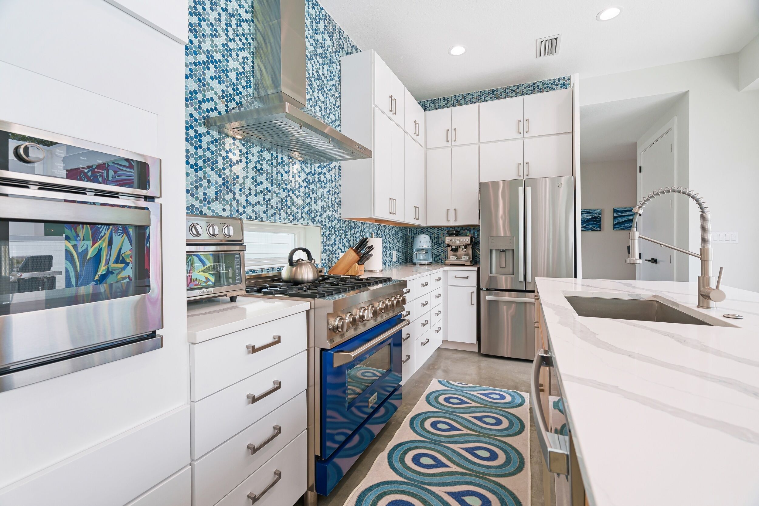 A modern kitchen with stainless steel appliances, white cabinetry, and a blue patterned backsplash.