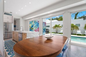 A modern kitchen with a wooden dining table, a refrigerator, and a view of a swimming pool. - Paradise Found 3 Bedroom Home by RedAwning (Sarasota)