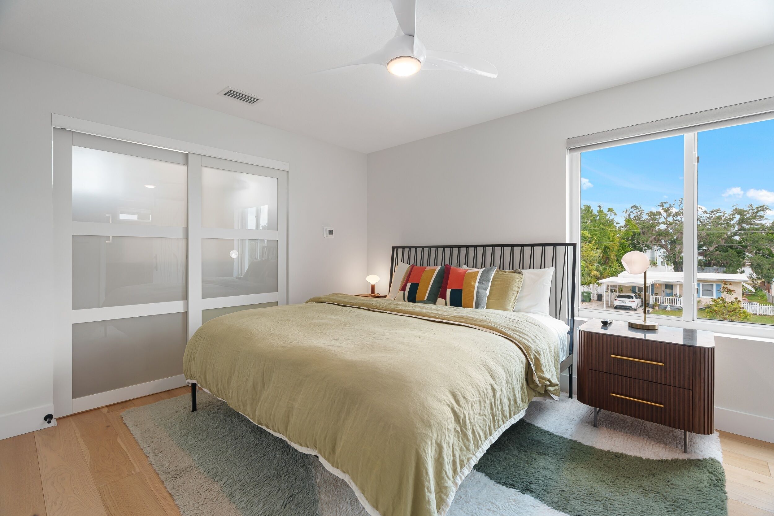 A bedroom with a bed, a nightstand, a window with a view, and a ceiling fan.