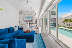Una sala de estar moderna con un sofá seccional azul, un televisor de pantalla plana y vistas a una piscina.
