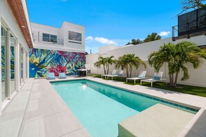A modern outdoor pool area with a colorful mural, lounge chairs, and palm trees. - Paradise Found 3 Bedroom Home by RedAwning (Sarasota)