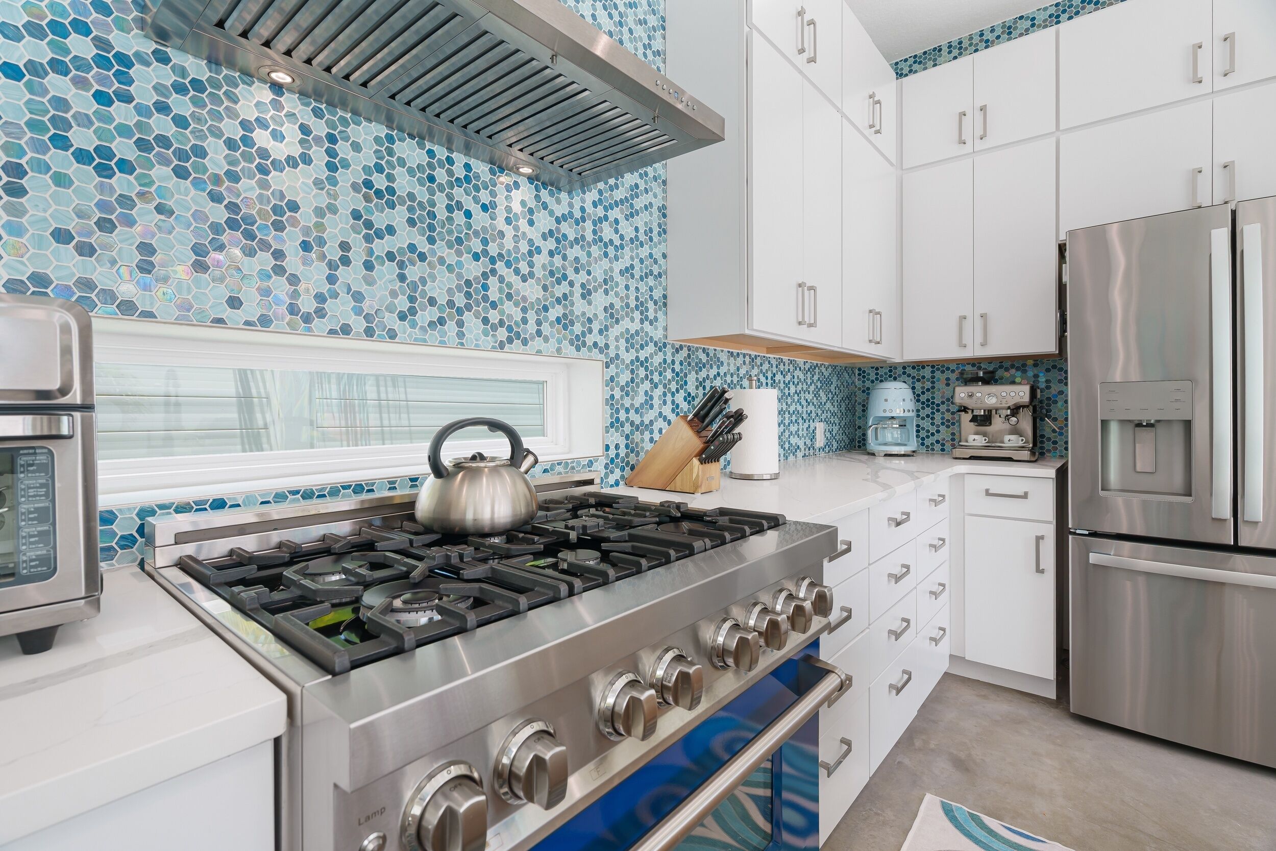 A modern kitchen with a gas stove, stainless steel appliances, and white cabinets.