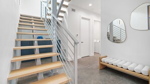 A modern staircase with wooden steps and a metal railing, leading to a room with a bench and a mirror on the wall. - Paradise Found 3 Bedroom Home by RedAwning (Sarasota)
