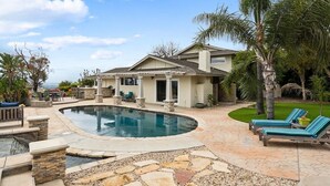Une maison avec une piscine, une terrasse en pierre et des chaises longues.
