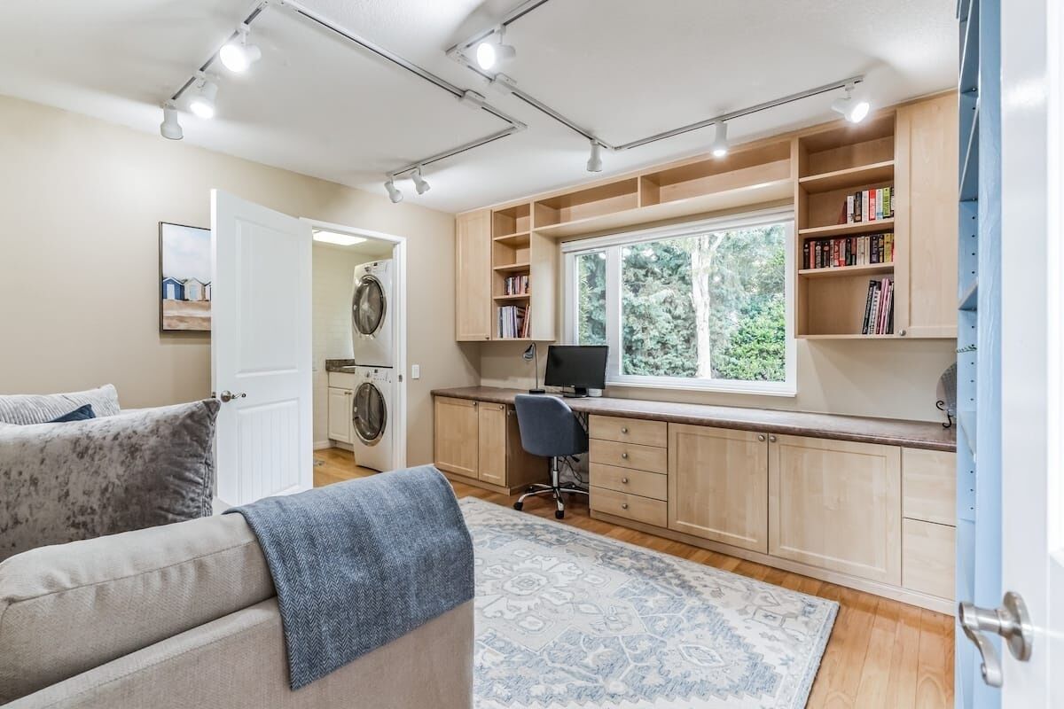 A compact living space with a kitchenette, a washing machine, a computer desk, and a sofa.