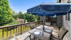 A wooden deck with a table set for dining, a blue umbrella, and a view of a garden and pool. - Bear Pass - Mountain View 4 Bedroom Home by RedAwning (Arlington)