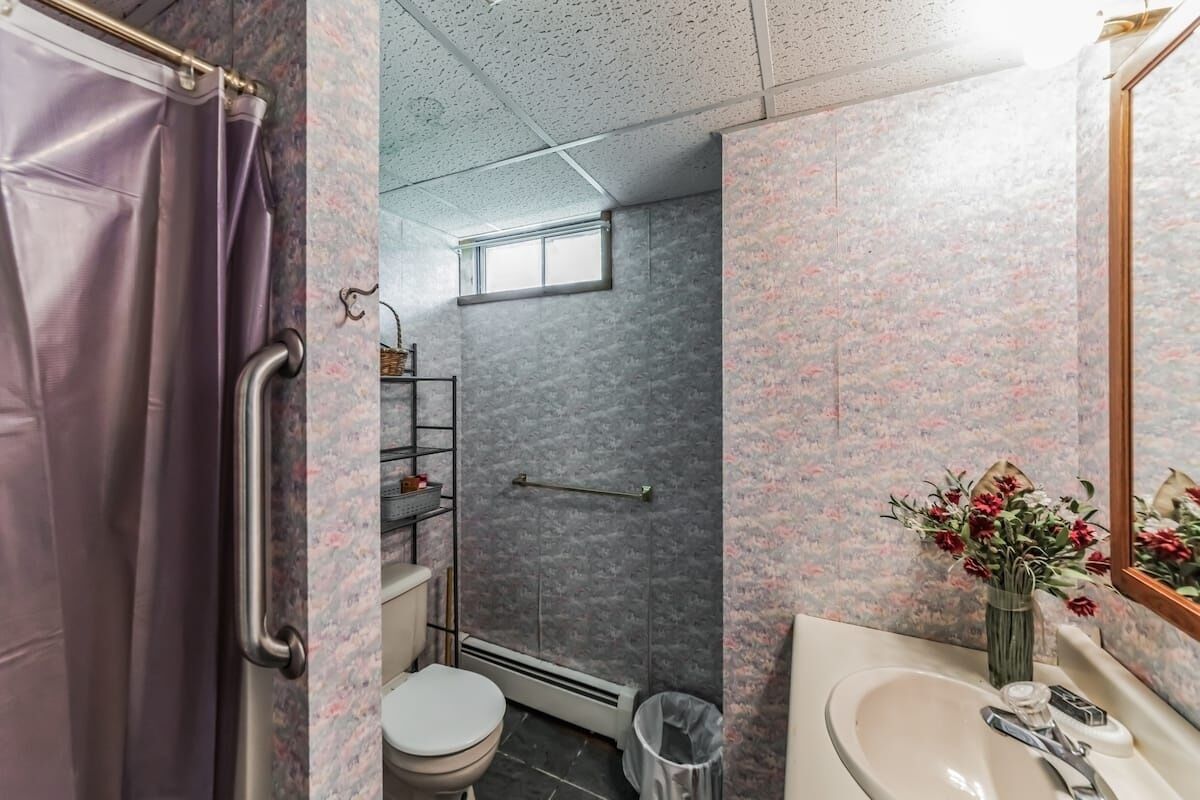 Een badkamer met douche, toilet en wastafel, met een behangpatroon met bloemen en een klein raam.