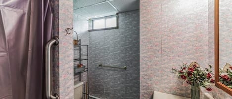 Een badkamer met douche, toilet en wastafel, met een behangpatroon met bloemen en een klein raam.