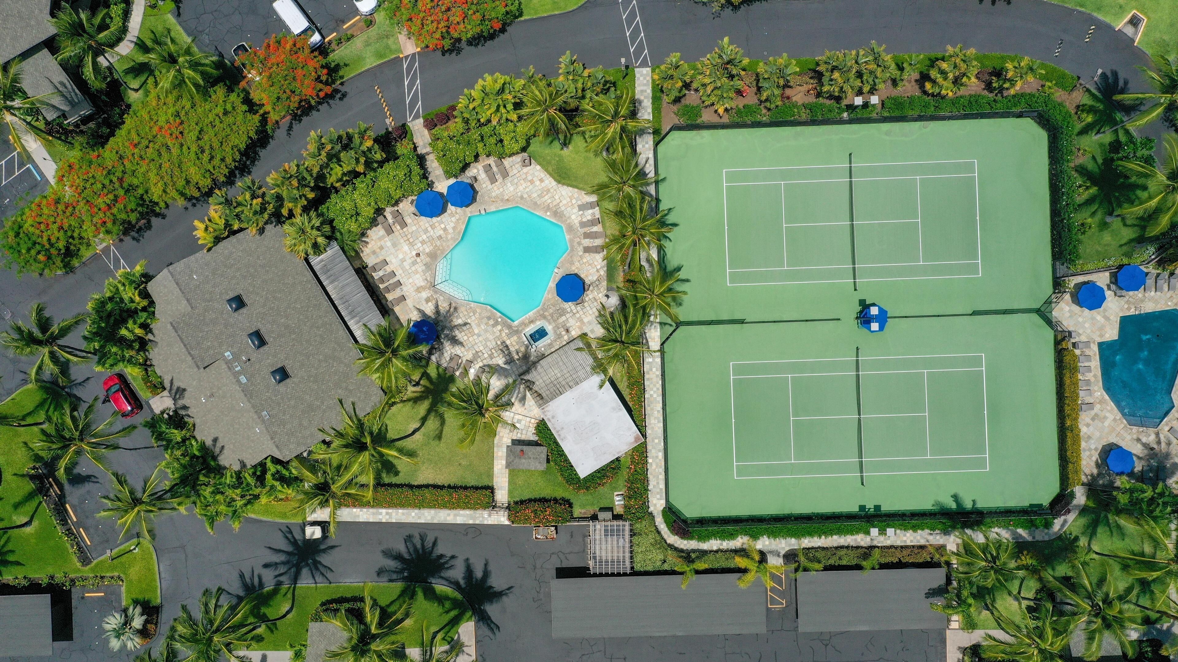 An aerial view of a resort with a tennis court, a swimming pool, and lush landscaping.