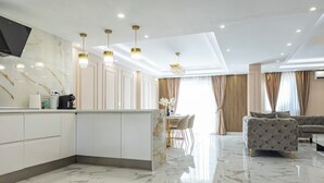 Een moderne keuken met marmeren werkbladen, een eetgedeelte met een kroonluchter, en een woonkamer met een bank.