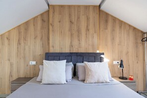 Ein Schlafzimmer mit schrägen Wänden, Holzvertäfelung, einem Bett mit weißer Bettwäsche, einer Nachttischlampe und einem kleinen Tisch mit einer Kerze.