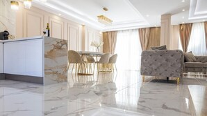 Een moderne woonkamer met een marmeren vloer, een eethoek met een glazen tafel en een bank met een gestuikte bekleding.