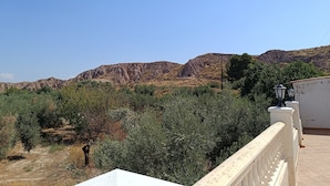 A balcony with a view of a mountainous landscape, a white railing, and a building with a red roof. - The Terrance Principle Asturias 15 (Guadix)
