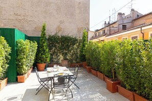 A patio with a table and chairs, surrounded by potted plants and a green fence. - The Incredible Domus Ruspoli (Roma)