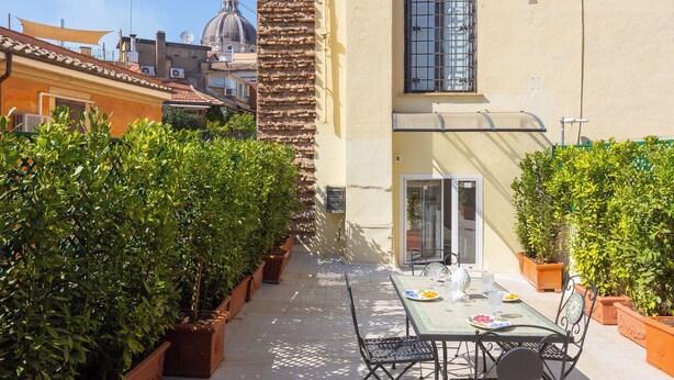 A patio with a table and chairs, surrounded by potted plants. - Amazing Domus Ruspoli  (Roma)