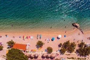Vista aérea de una playa con agua turquesa cristalina, gente nadando y sombrillas de playa.