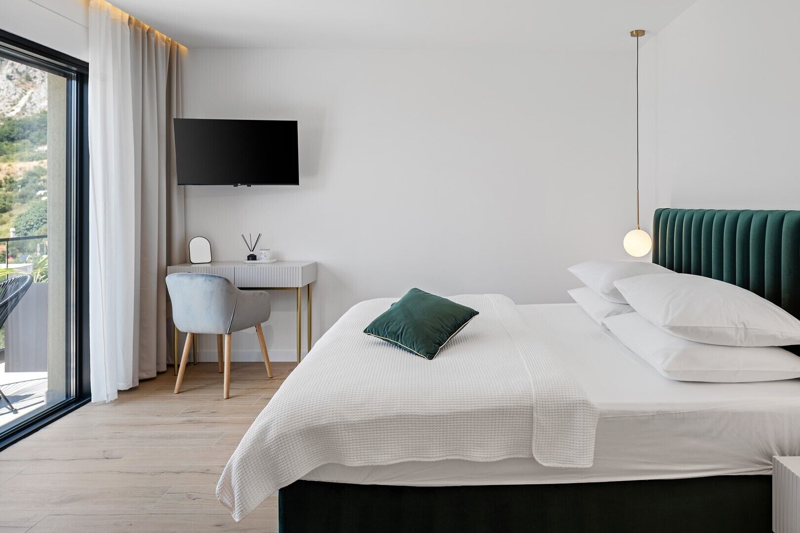 Un dormitorio moderno con cama, escritorio, silla, televisor y vistas al balcón.