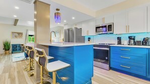 A modern kitchen with blue cabinets, a central island, and gold bar stools.