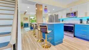 A modern kitchen with blue cabinets, stainless steel appliances, and gold bar stools.