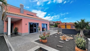 Een roze gebouw met een betegeld dak, een overdekte patio en een tuin met potplanten.