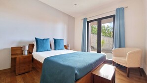 Een slaapkamer met een bed, twee nachtkastjes, een stoel en een groot raam met gordijnen.