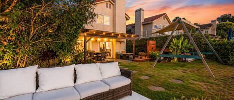Eine Terrasse mit Rattan-Sofa, einer Schaukel und einem Haus mit überdachter Veranda.
