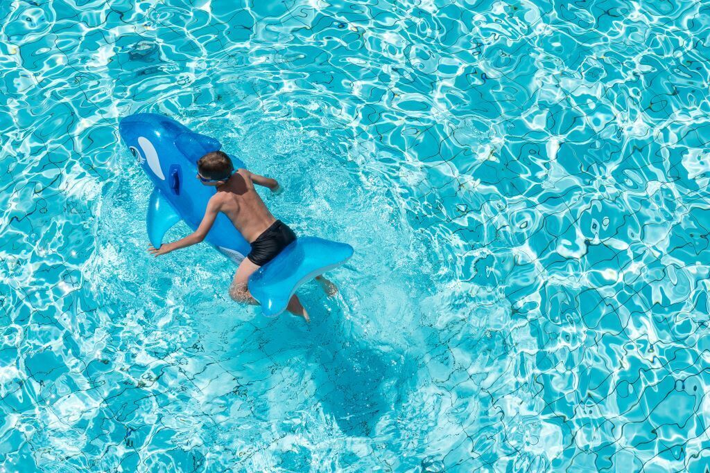Une personne dans une piscine, sur un flotteur gonflable en forme de requin bleu.