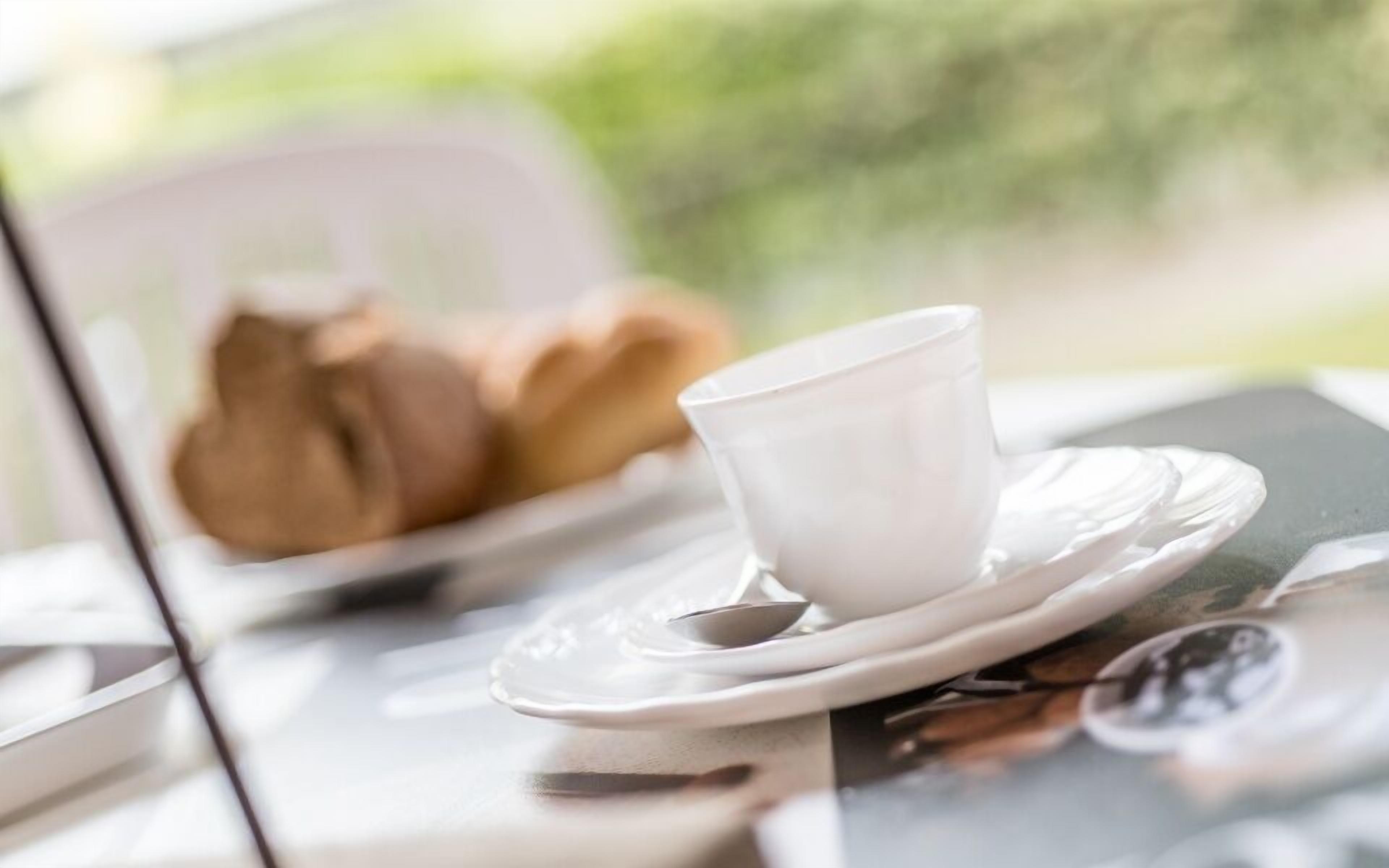 A table with a white cup and saucer, a spoon, and a plate with a pastry.