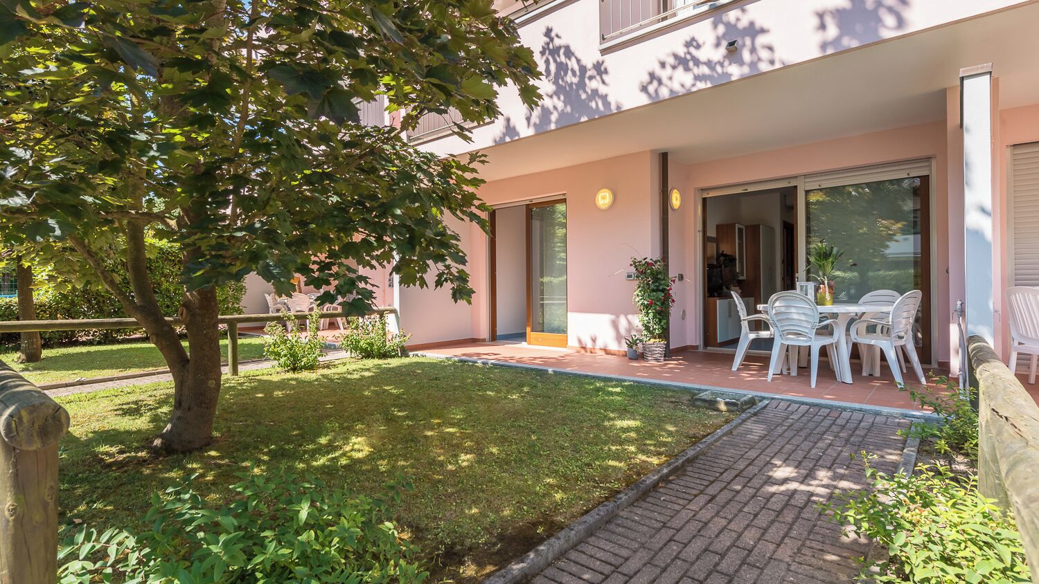 A patio area with a table and chairs, a small garden, and a building entrance.