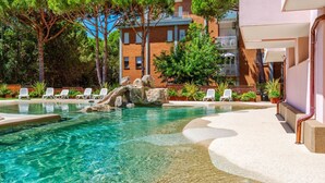 A clear swimming pool with a rock feature, surrounded by lounge chairs and potted plants. - COSTA RICA BIBIONE Eco Resort (San Michele al Tagliamento)