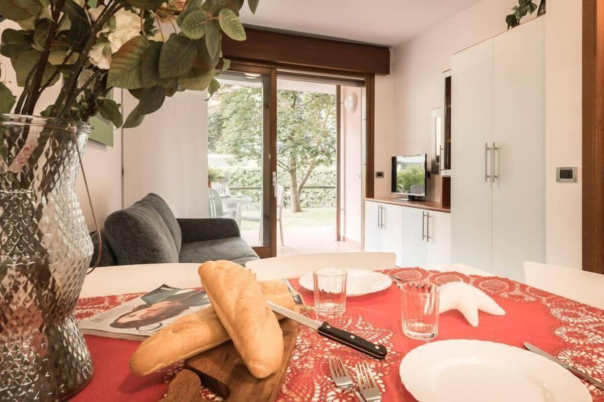 Un comedor con mantel rojo, un jarrón con hojas verdes y una tabla de madera con pan.