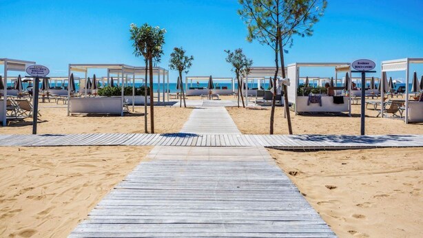 A beach resort with a wooden walkway leading to beach umbrellas and lounge chairs. - COSTA RICA BIBIONE Eco Resort (San Michele al Tagliamento)