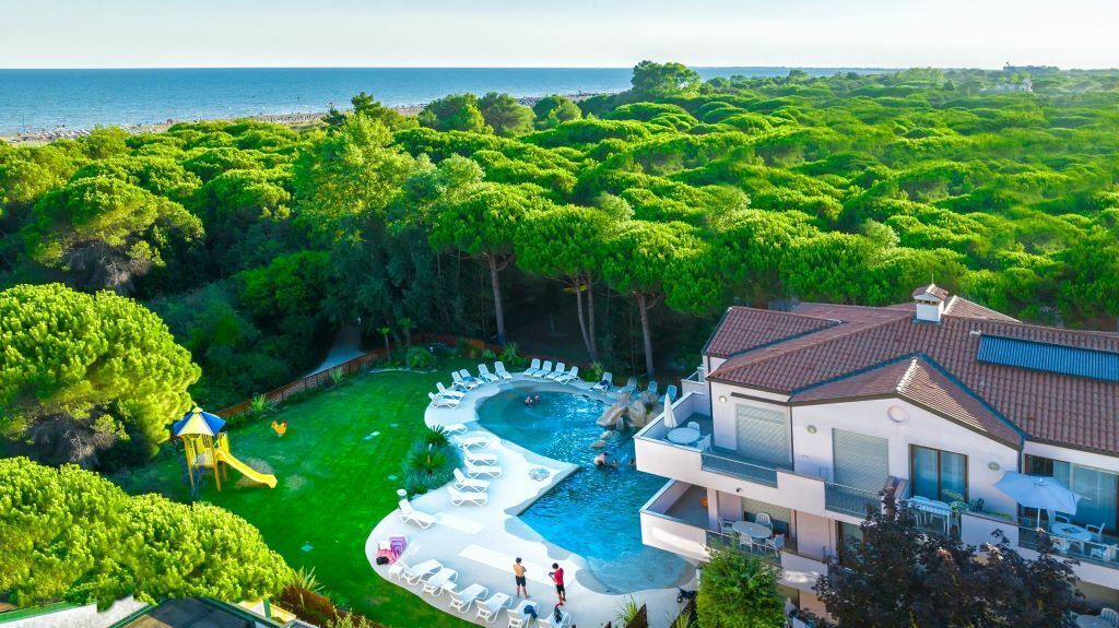 A modern hotel with a swimming pool surrounded by lush greenery and a view of the sea.