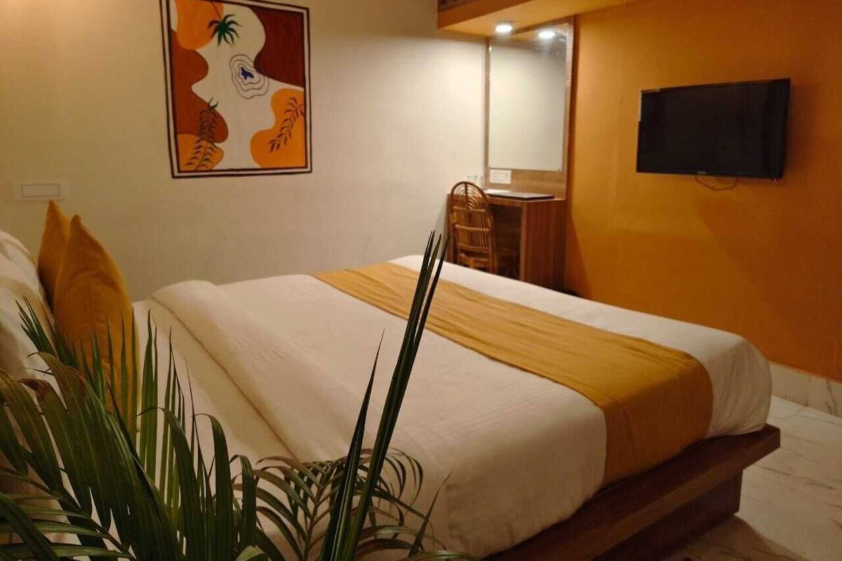 A hotel room with a bed, a television mounted on the wall, and a painting above the bed.