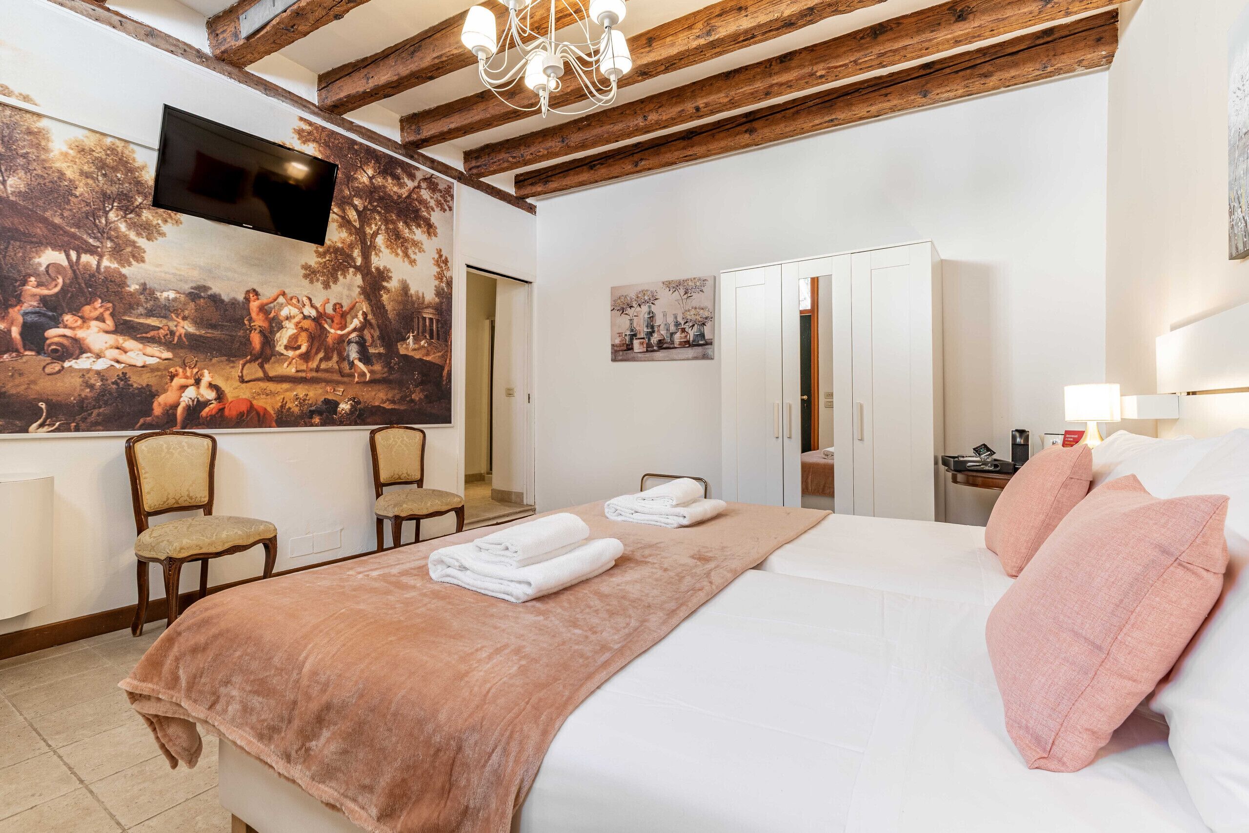 A hotel room with a large bed, a TV mounted on the wall, a painting, and a wooden ceiling.