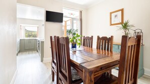 Un comedor con una mesa y sillas de madera, una planta en maceta y un cuadro en la pared.