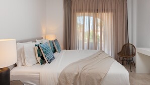 A hotel room with a large bed, a chair, a desk, and a window with curtains. - Bright 3BR with Sunset Views and Garden (Benahavís)