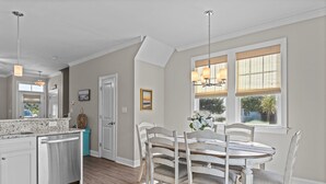 Une cuisine moderne dotée d’un îlot central, d’un coin repas avec des chaises blanches et d’une grande fenêtre équipée de stores.