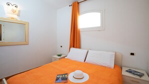 A bedroom with an orange bedspread, a white hat, and a book on the nightstand.