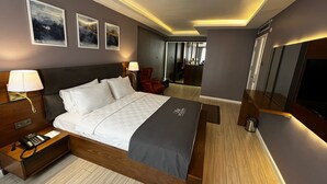 Una habitación de hotel moderna con una cama grande, mesitas de noche, un escritorio, una silla, un televisor y obras de arte en las paredes.