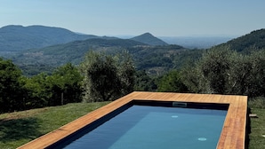 A rectangular swimming pool with a wooden deck, surrounded by a grassy area and overlooking a mountainous landscape. - Typical Stone House with Swimming Pool 6/8 Pax in the countryside between Florence and Lucca. (marliana)