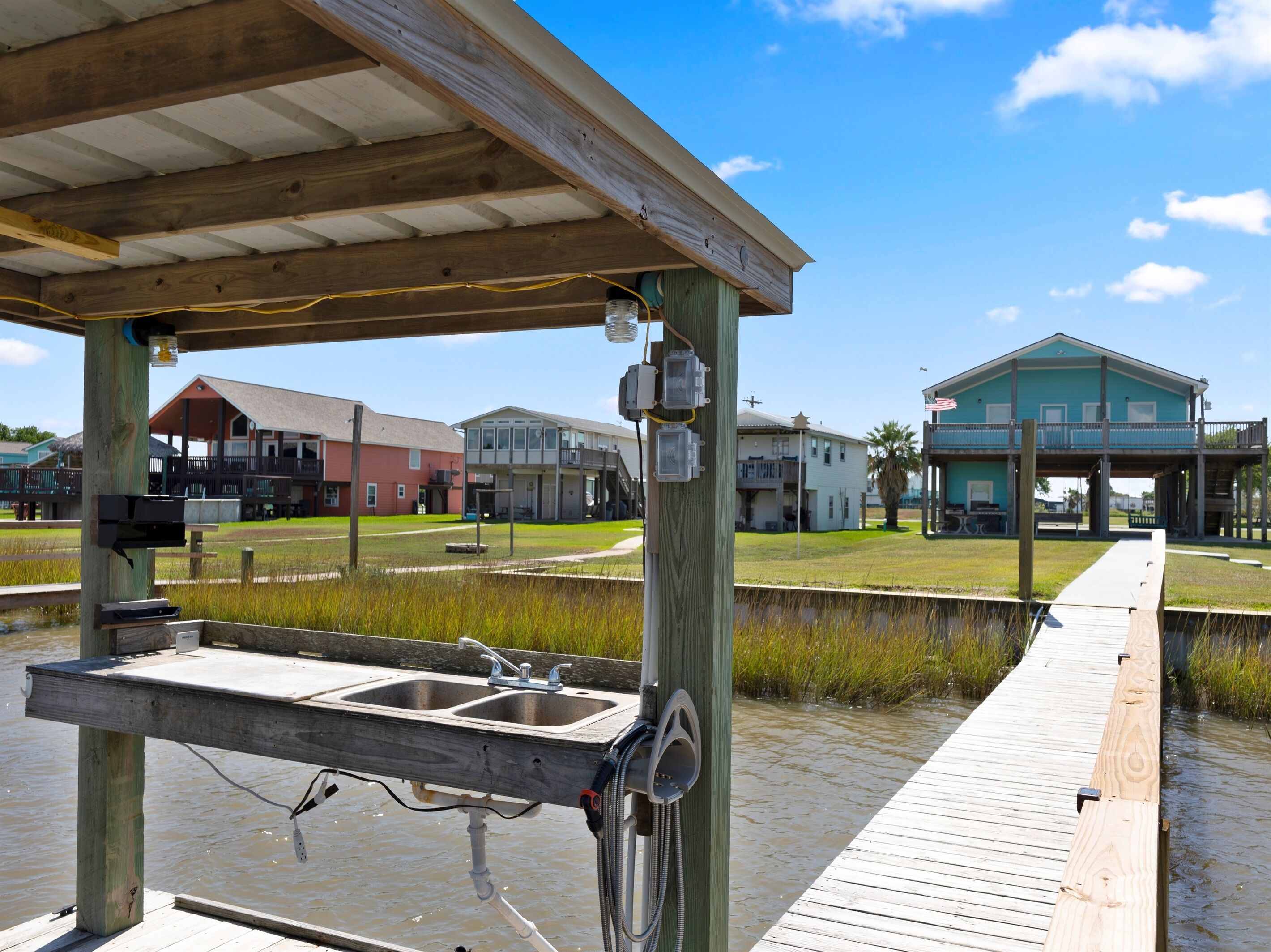 Un muelle de madera con un lavadero metálico y una manguera, que conduce a un embarcadero sobre el agua.