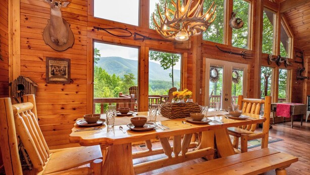 A wooden cabin with a dining table set for four, surrounded by wooden chairs. - *Gorgeous 3BD Cabin w/ VIEWS! Hot Tub + Fire Pit!* (Sevierville)