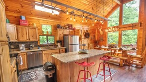 A wooden cabin kitchen with a central island, bar stools, and a large window overlooking greenery. - *Gorgeous 3BD Cabin w/ VIEWS! Hot Tub + Fire Pit!* (Sevierville)