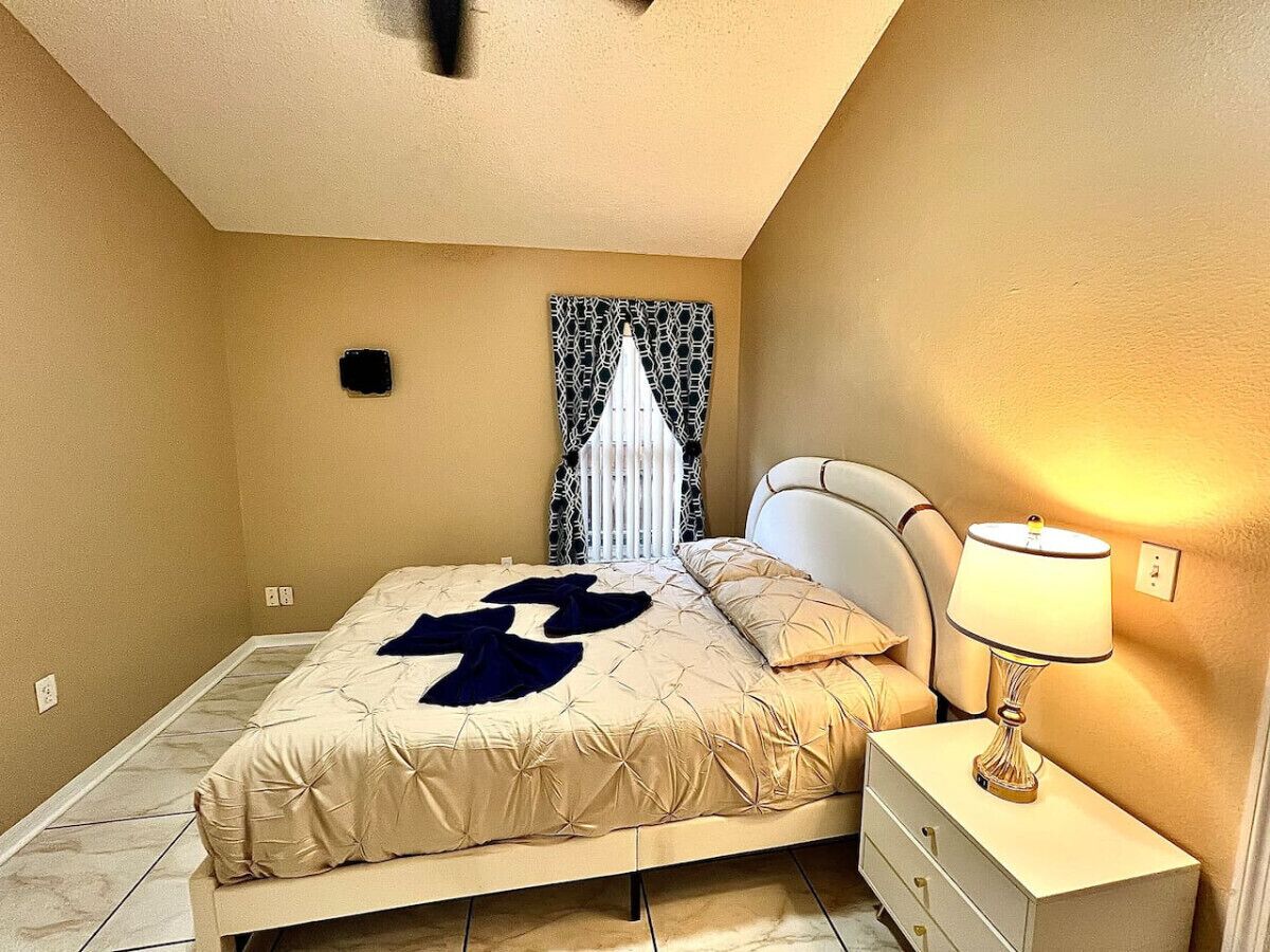 Une chambre à coucher avec un lit, une table de chevet, une lampe et une fenêtre ornée de rideaux à motifs.
