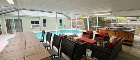 Un patio exterior con piscina, mesa de comedor, sillas y mobiliario de mimbre.