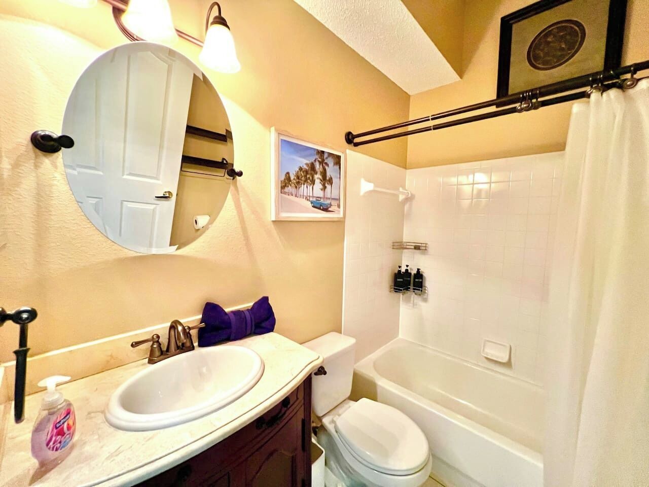 Un baño con un lavabo blanco, un inodoro y una bañera. Hay un espejo sobre el lavabo y un cuadro enmarcado en la pared.