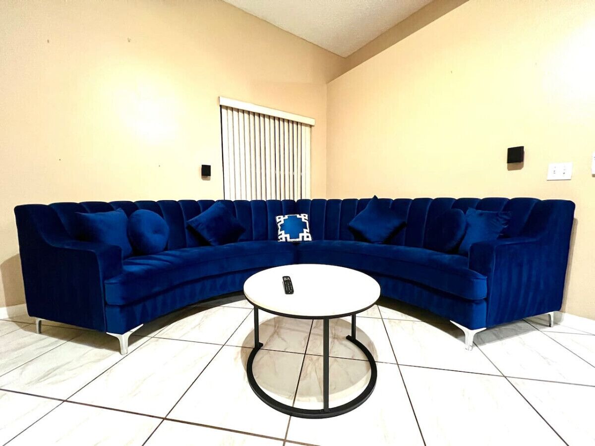Un salon avec un canapé d’angle bleu, une table basse ronde et un sol blanc.