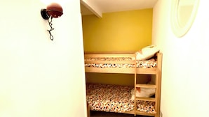 A narrow hallway with a bunk bed in the center, a wall-mounted light fixture, and a small mirror on the right wall.